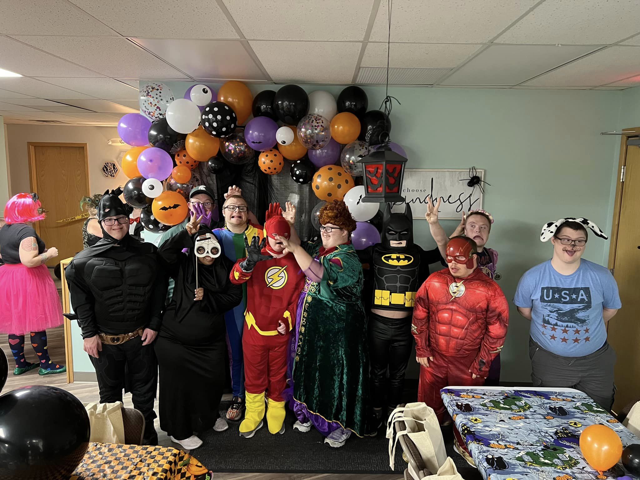 A group of young adults with Down syndrome dressed in Halloween costumes and posing in front of a balloon arch.